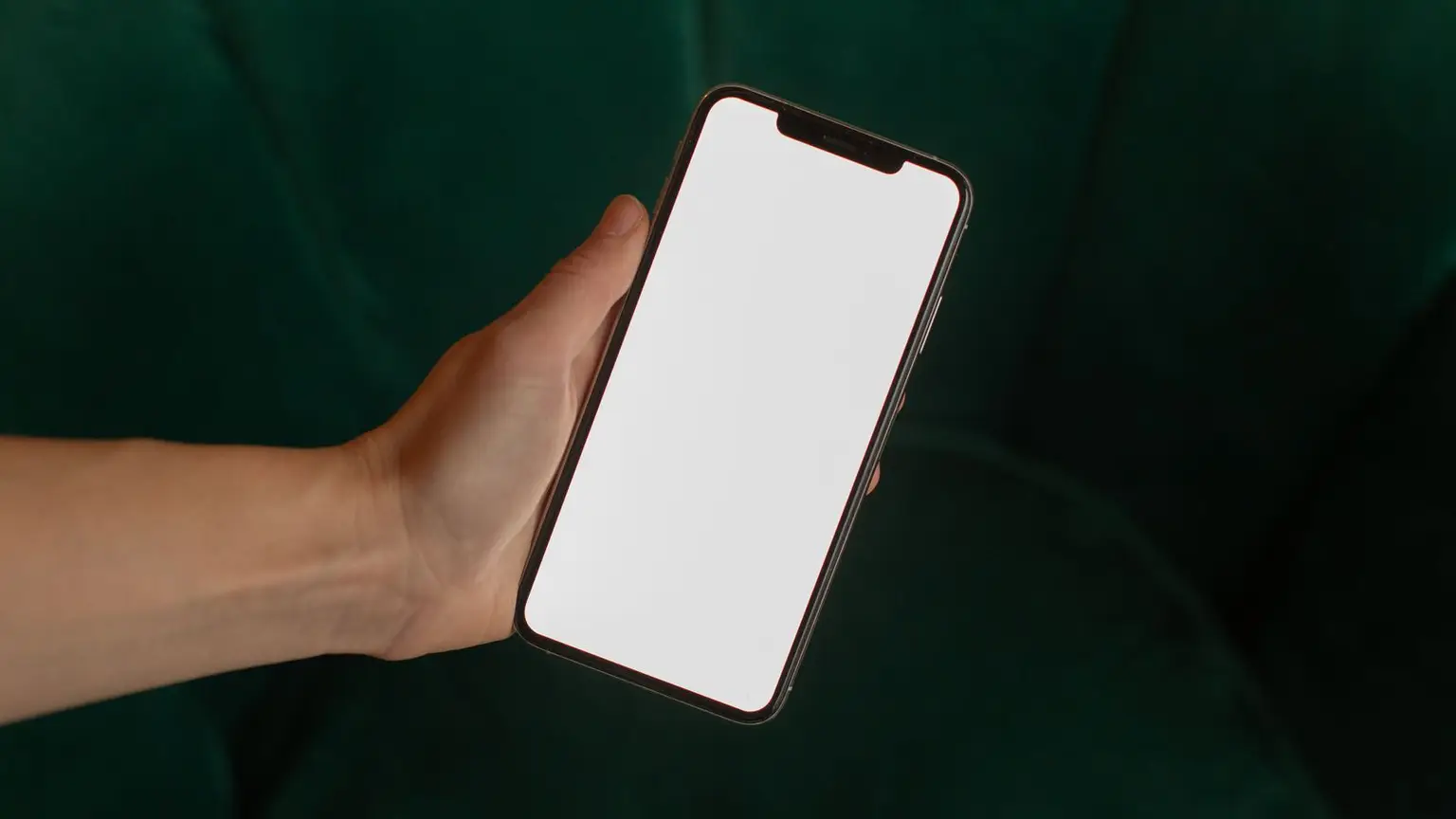 Koyu yeşil bir zeminin önünde, ekranı boş bir akıllı telefonu tutan el